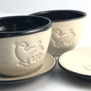 Black and white ceramic bowl/cup with a swirly dove on the front with a cover plate saucer also debossed with the same design